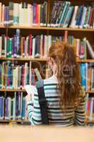 Redhead student reading book from shelf standing in library