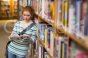 Redhead student reading book leaning on shelf in library