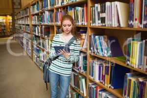 Focused student using tablet leaning on shelf in library