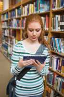 Redhead student using tablet standing in library