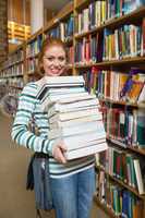 Cheerful student holding heavy pile of books standing in library