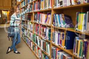 Redhead student taking book from shelf in the library