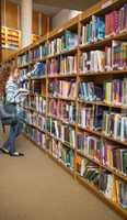 Redhead student taking a book from bookshelf in the library