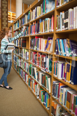 Redhead student taking book from bookshelf in the library