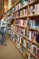 Redhead student taking book from bookshelf in the library