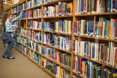 Redhead student taking a book from library bookshelf