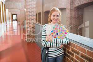 Young student smiling at camera in the hall holding folders