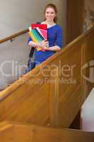 Cheerful student holding folders on the stairs looking at camera