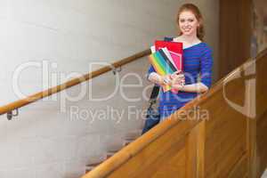 Redhead student holding folders on the stairs smiling at camera
