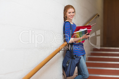 Smiling young student holding her notes on the stairs