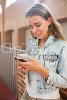 Cheerful student standing in the hall sending a text