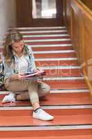 Pretty young student sitting on stairs looking at camera