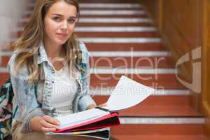Smiling young student sitting on stairs looking at camera