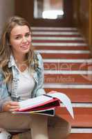 Cheerful young student sitting on stairs looking at camera