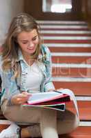 Cheerful young student sitting on stairs reading notes