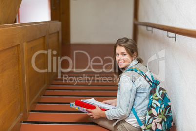 Happy young student sitting on stairs looking up at camera