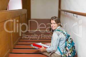 Happy young student sitting on stairs looking up at camera