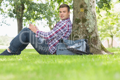 Smiling student using his tablet to study outside