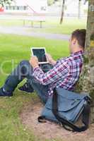 Student using his tablet pc outside leaning on tree