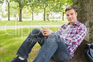 Cheerful student sending a text outside leaning on tree