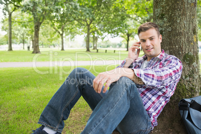 Happy student on the phone outside leaning on tree