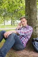Smiling student on the phone outside leaning on tree