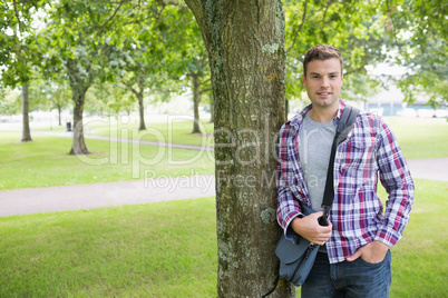 Smiling student leaning on tree looking at camera