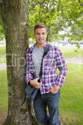 Happy student leaning on tree looking at camera