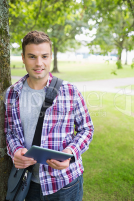 Handsome student leaning on tree looking at camera holding table