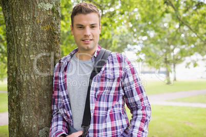 Handsome young student leaning on tree looking at camera