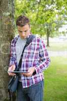Focused student leaning on tree using his tablet pc