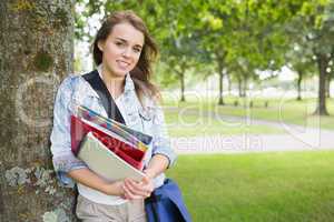 Smiling student leaning on tree holding her books