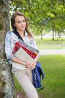 Happy student leaning on tree holding her books