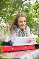 Cheerful student lying on the grass studying with her tablet pc