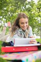 Pretty student lying on the grass studying with her tablet pc