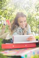 Pretty young student lying on the grass studying with her tablet