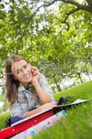 Young smiling student lying on the grass on the phone