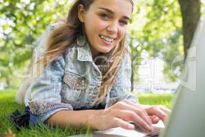 Young smiling student lying on the grass using laptop