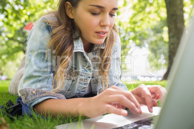 Young focused student lying on the grass using her laptop