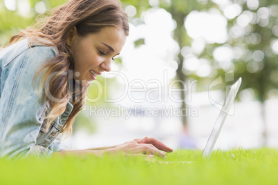 Happy student lying on the grass using her laptop