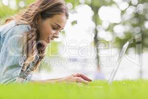 Happy student lying on the grass using her laptop