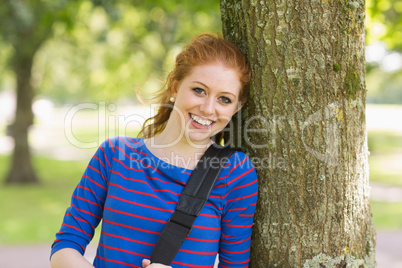 Happy redhead student leaning on tree looking at camera