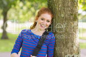 Happy redhead student leaning on tree looking at camera