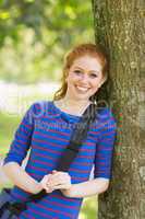Pretty redhead student leaning on tree looking at camera
