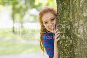 Smiling redhead hiding behind a tree