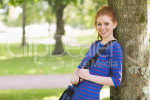 Cute redhead student leaning against a tree