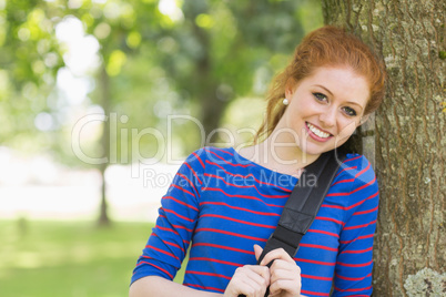 Cheerful redhead student leaning against a tree