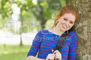 Cheerful redhead student leaning against a tree