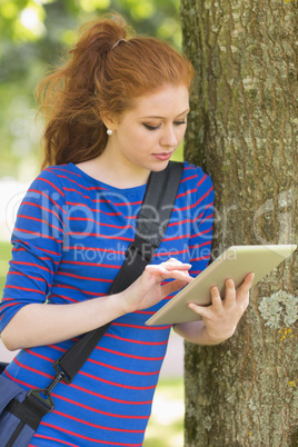 Cheerful student leaning against a tree using her tablet