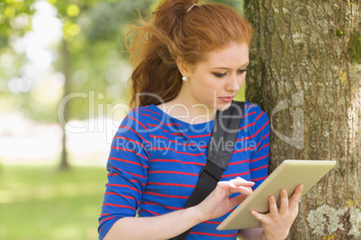 Redhead student leaning against a tree using her tablet